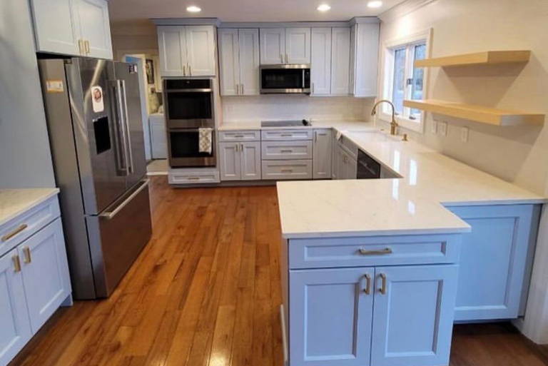 Modern kitchen with stainless steel appliances, white countertops, wooden floor, and white cabinets