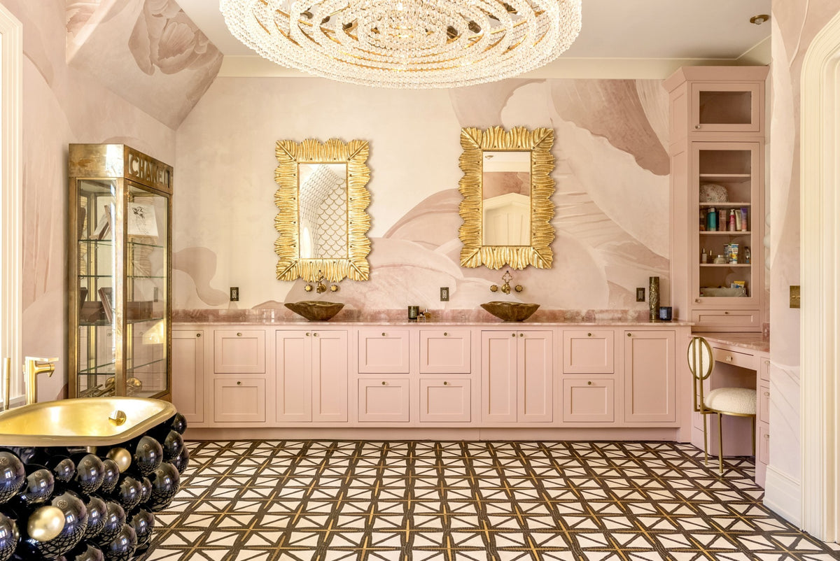 Image of gorgeous bathroom with light pink Gracious Home Custom cabinets and golden leaf mirrors on the wall along with beautiful chandelier hanging down