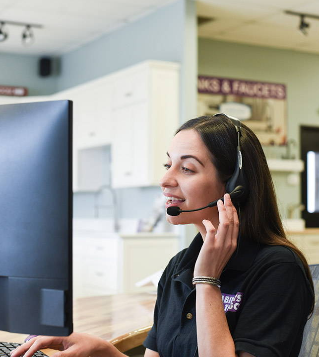 Image of female customer service representative for Cabinets To Go on a wireless call with customer while looking at desktop computer.
