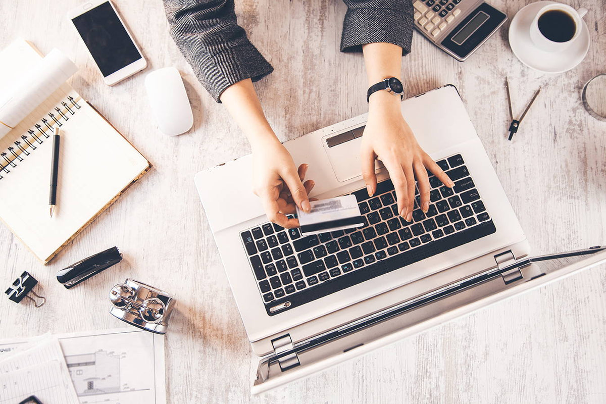 Person using a laptop with a credit card on a desk with office supplies.