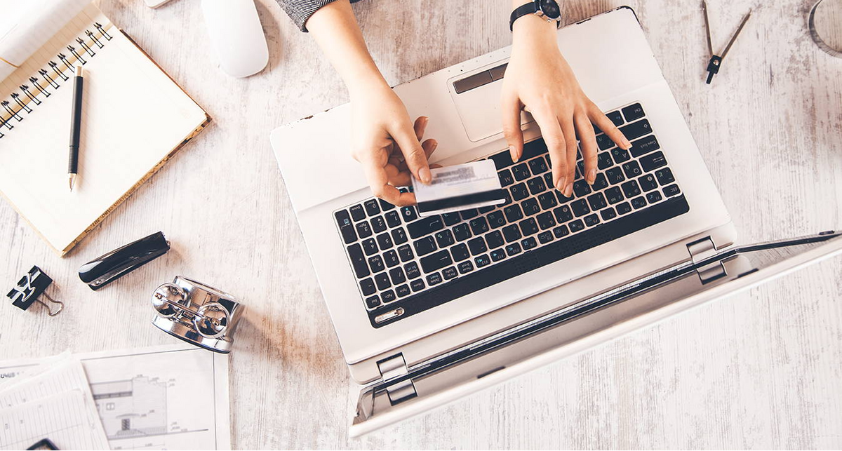 Person using a laptop with a credit card on a desk with office supplies.